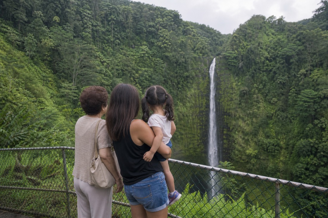Three generations of one family at the fenced main overlook watching Akaka Falls