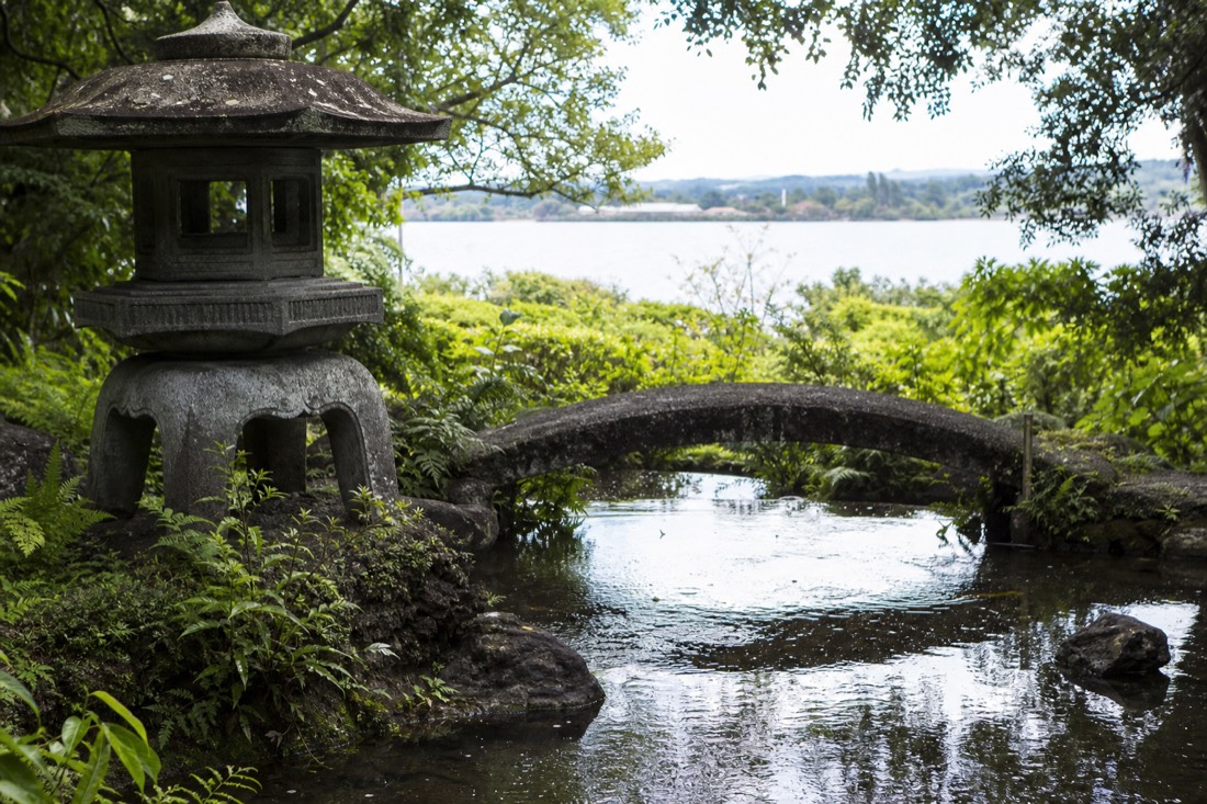 Stone lantern and arched footbridge over a fishpond at Liliuokalani Gardens with Hilo Bay behind