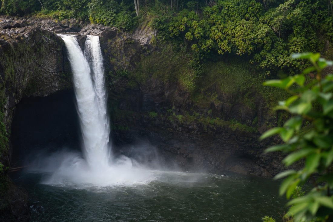 Rainbow Falls pouring over its dark ledge into a green pool with mist rising in morning light